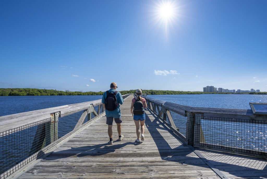 People walking on the boardwalk leading to Atlantic ocean. Friends hiking on the pathway over the lake. John D. MacArthur Beach State Park, North Palm Beach, Florida. USA. Copy space.