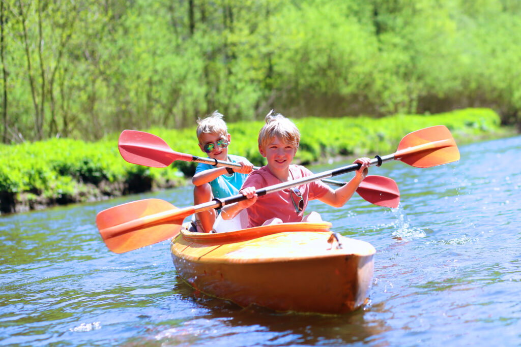 Two boys kayaking on the river. Active happy friends, teenage schoolboys, having fun together enjoying adventurous experience with kayak on a sunny day during summer vacation