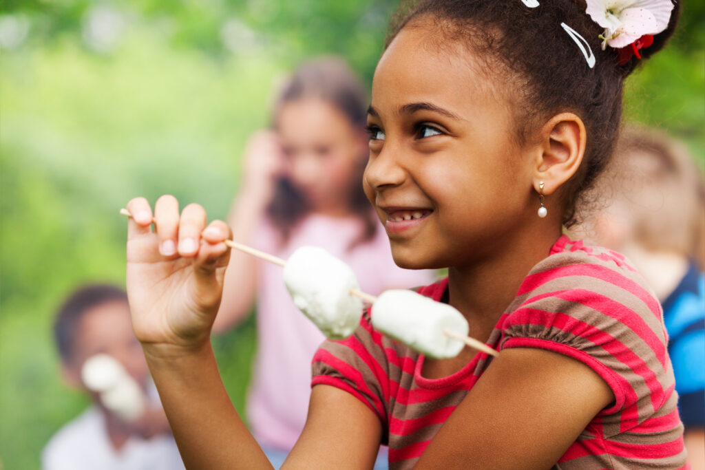 Portrait of African girl holding stick with marshmallow during camping in the forest with other kids