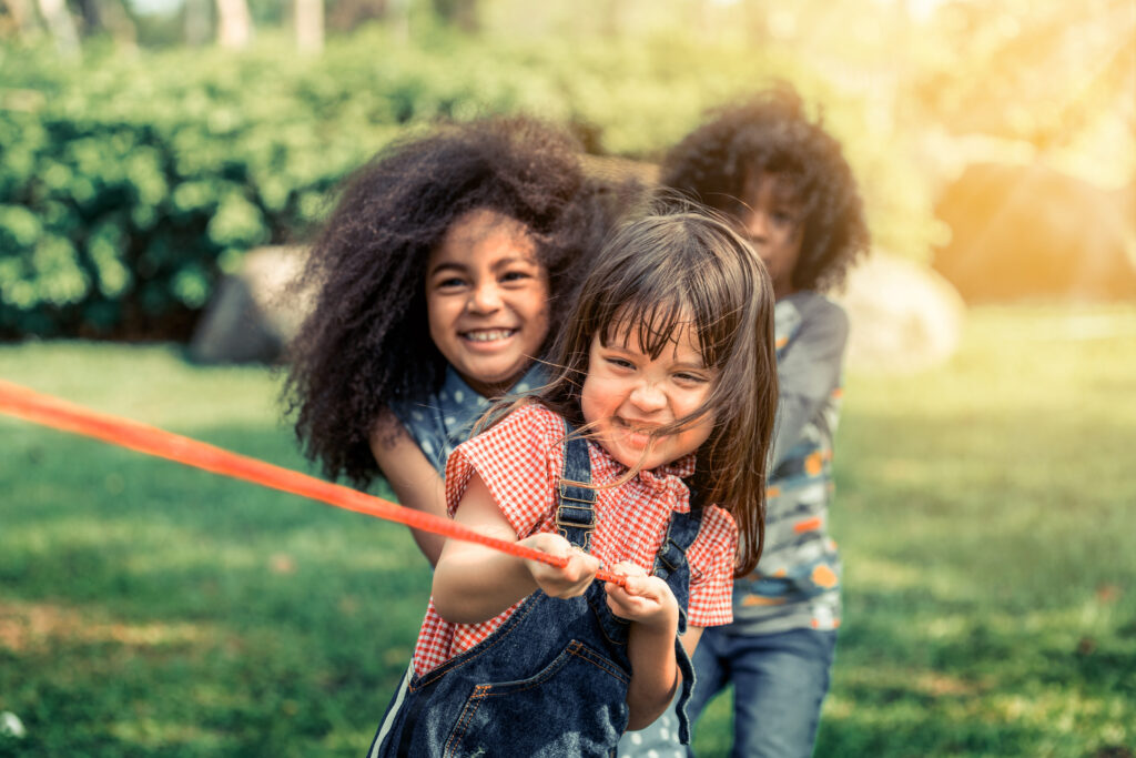 Happy children playing tug of war and having fun during summer camping in the park. Children recreation concept.