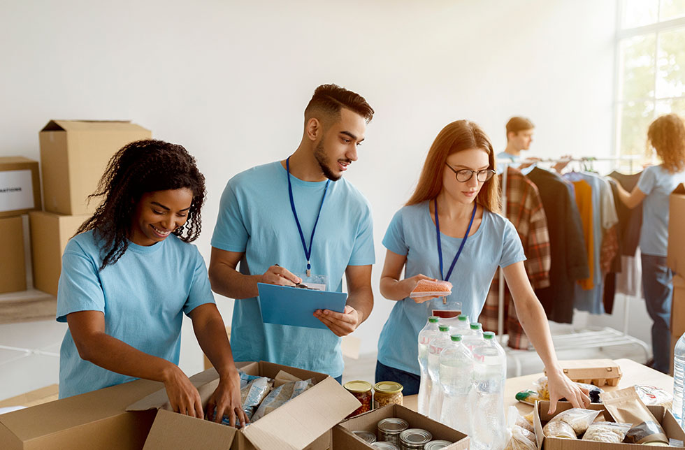 Young group of multiracial volunteers working in community charity donation center, sorting donated food in boxes, preparing boxes for poor and homeless people
